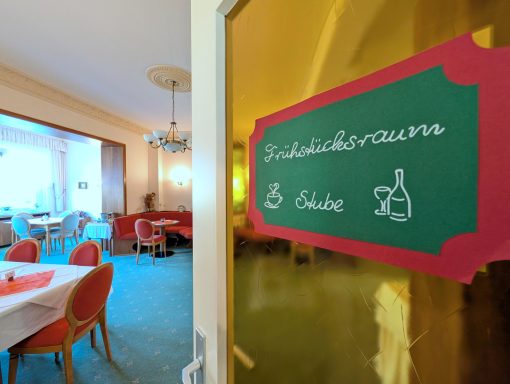 Eingang zum Frühstücksraum mit Tisch und roten Stühlen im Hintergrund.