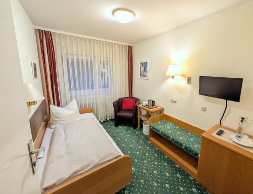 Ein einfaches Hotelzimmer mit einem Bett, einem Stuhl, einem Tisch und einem Fernseher.