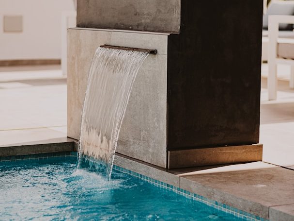 Wasserfall, der in einen modernen Pool mit hellem Rand fließt.