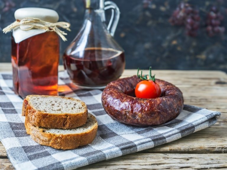 Brot, Wurst, Tomate und eine Flasche Sirup auf einem karierten Tuch.
