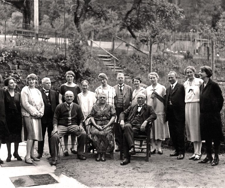 Gruppenszene mit mehreren Menschen im Freien, einige sitzen, andere stehen, schwarz-weiß.