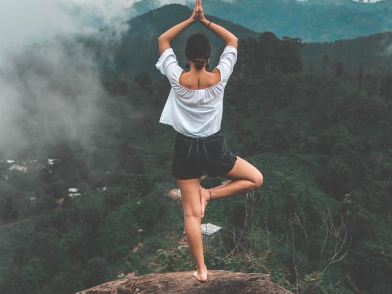 Person in Yoga-Pose auf einem Felsen, umgeben von Bergen und Nebel.