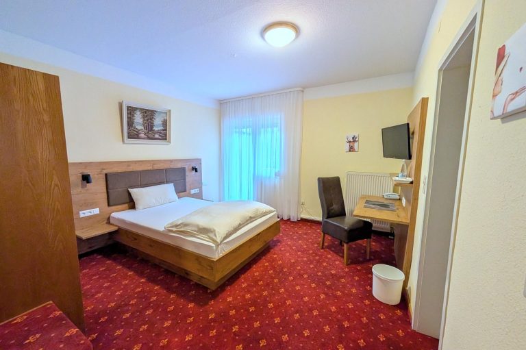 Ein einfaches Hotelzimmer mit Einzelbett, Schreibtisch und Fernseher.