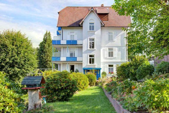 Weißes Hotel mit blauen Balkonen und gepflegtem Garten.