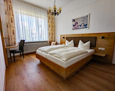 Helles Hotelzimmer mit Doppelbett, Tisch und Stuhl, Holzverkleidung und Fenster.