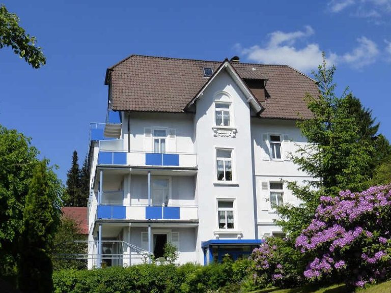 Weißes Hotel mit Balkon und gepflegtem Garten im Vordergrund.