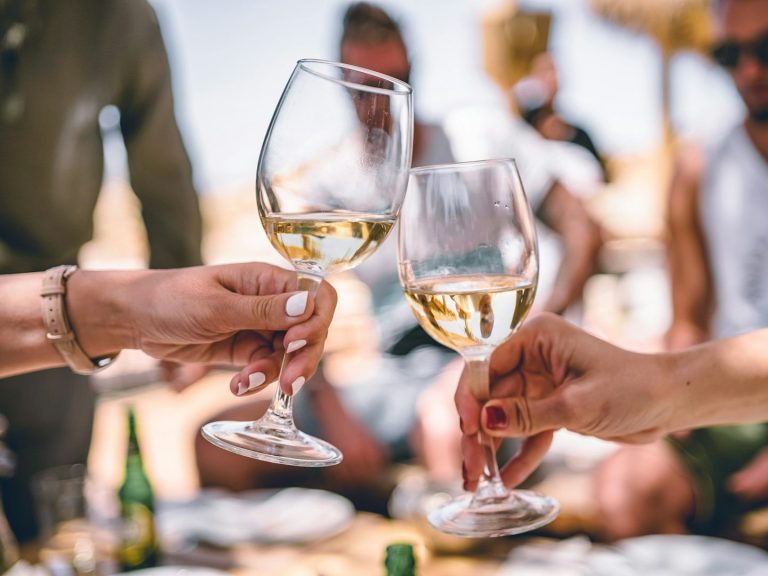 Gläser mit Weißwein werden beim Anstoßen in einer geselligen Runde gehalten.