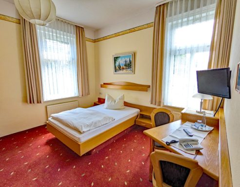 Helles Einzelzimmer mit Bett, Schreibtisch und Fenster, dekoriert mit einem Bild.