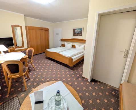 Helles Hotelzimmer mit zwei Einzelbetten, Tisch, Stühlen und einem Kleiderschrank.