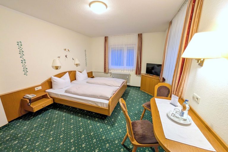 Helles Hotelzimmer mit zwei Betten, Tisch, Stühlen und Fernseher.