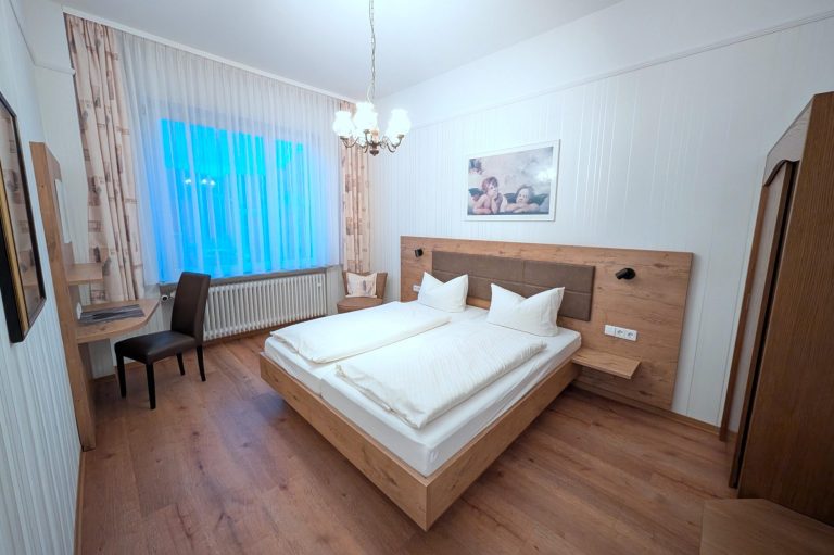 Helles Hotelzimmer mit zwei Einzelbetten, Schreibtisch und großer Fensterfront.