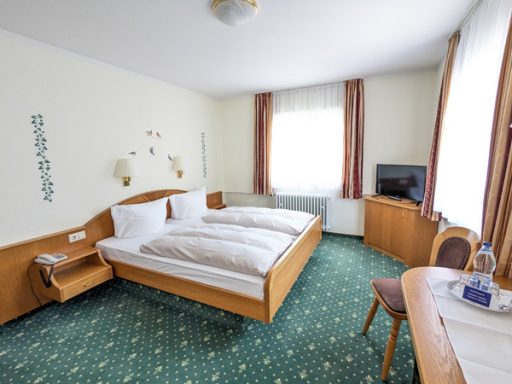 Helles Hotelzimmer mit Doppelbett, Schreibtisch und Fernseher.
