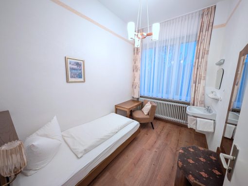 Helles Einzelzimmer mit Bett, Tisch, Stühlen und Fenster für Tageslicht.