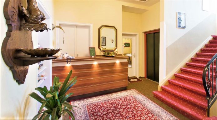 Rezeption mit Holztheke, Treppe und Pflanze, Teppich im Eingangsbereich.