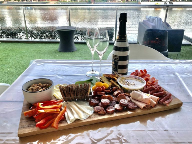 Brett mit Wurst, Käse, Paprika, Oliven, Nüssen und zwei Gläsern Champagner.