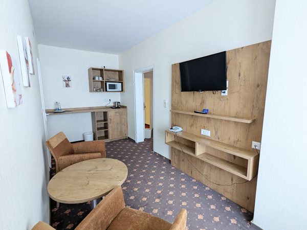 Heller Hotelzimmer mit Holzmöbeln, Sofa, Tisch und Flachbildfernseher.
