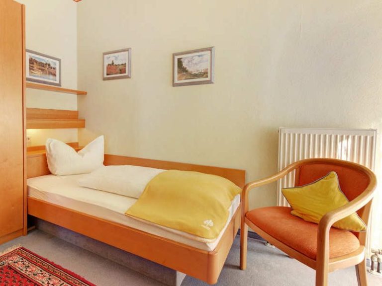 Ein helles Zimmer mit Einzelbett, Sessel und dekorativen Bildern an der Wand.
