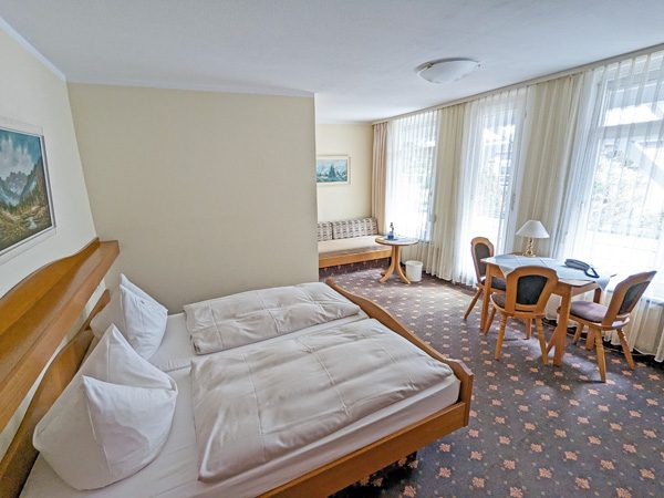 Helles Hotelzimmer mit zwei Betten, Tisch und Stühlen. Fenster sorgen für Tageslicht.