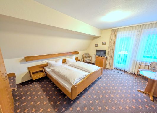 Helles Hotelzimmer mit zwei Einzelbetten, Tisch und Fernseher.
