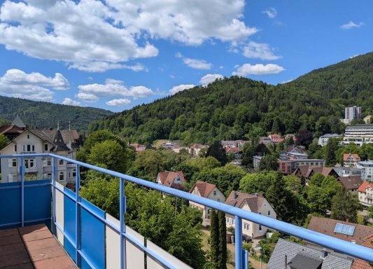 Aussicht von einem Balkon auf eine grüne Hügellandschaft mit Häusern.