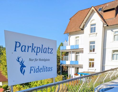 Schild mit der Aufschrift "Parkplatz nur für Gäste Fidelitas" vor einem Gebäude.