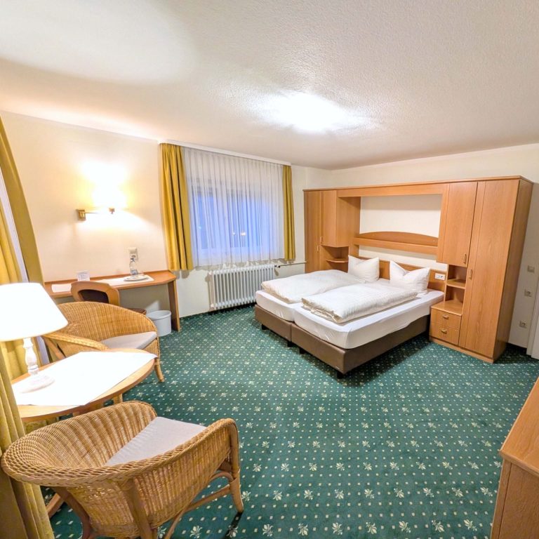 Helles Hotelzimmer mit zwei Betten, Sitzbereichen und Stühlen.