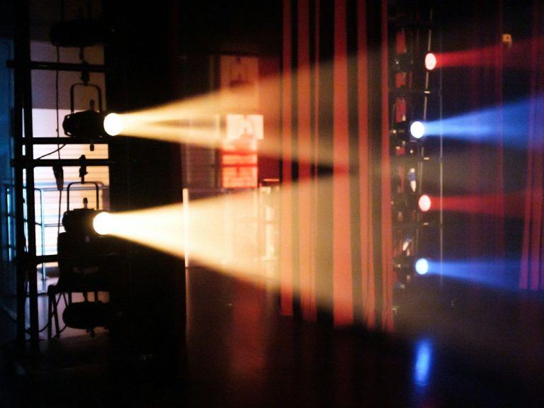 Bunte Lichtstrahlen leuchten auf eine Bühnenfläche in dunklem Raum.