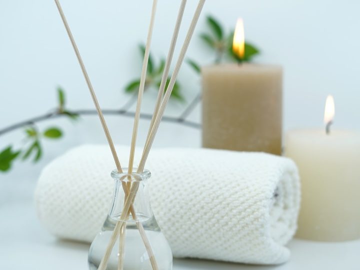 Diffusor mit Holzstäbchen, Kerzen und einem Handtuch auf einem hellen Hintergrund.