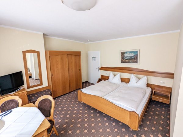 Helle Hotelzimmer mit Doppelbett, Tisch, Stühlen, Fernseher und Kleiderschrank.