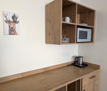 Moderne Kücheneinheit mit Holzregalen, Mikrowelle, Wasserkocher und Hirschbild an der Wand.