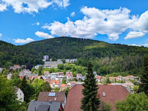 Blick auf eine grüne Hügelkette über einer Stadt mit bunten Häusern und blauen Himmel.