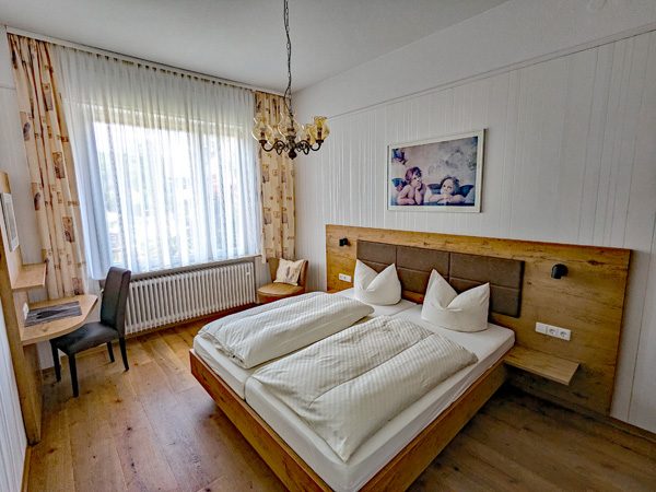 Helles Schlafzimmer mit Doppelbett, Holzdetails und Arbeitsbereich.