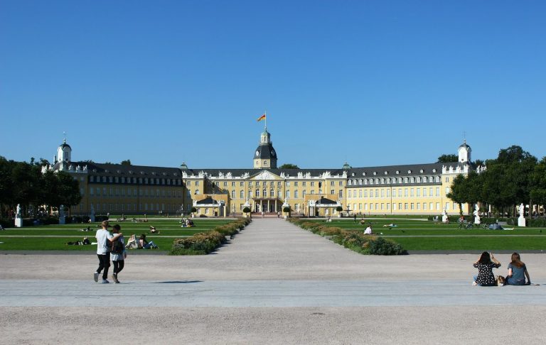 Schloss Karlsruhe mit Gartenanlage und blauem Himmel im Hintergrund.